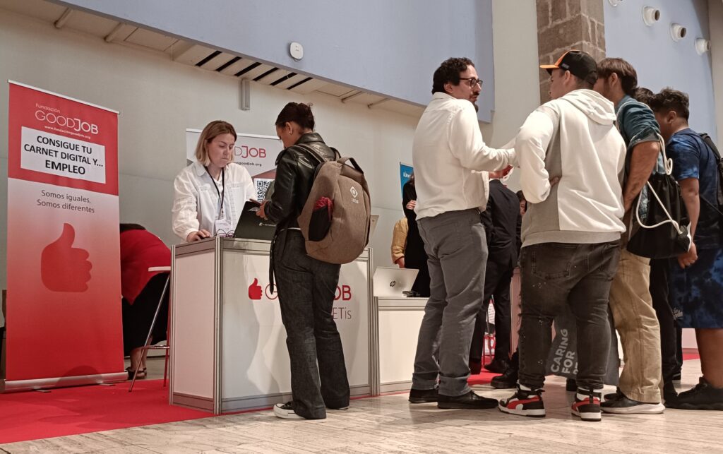 Participantes en el stand de Fundación GoodJob interactuando con los organizadores en la 9ª Feria de Discapacidad y Empleo de Barcelona, buscando oportunidades de empleo y recursos como el Carnet Digital.