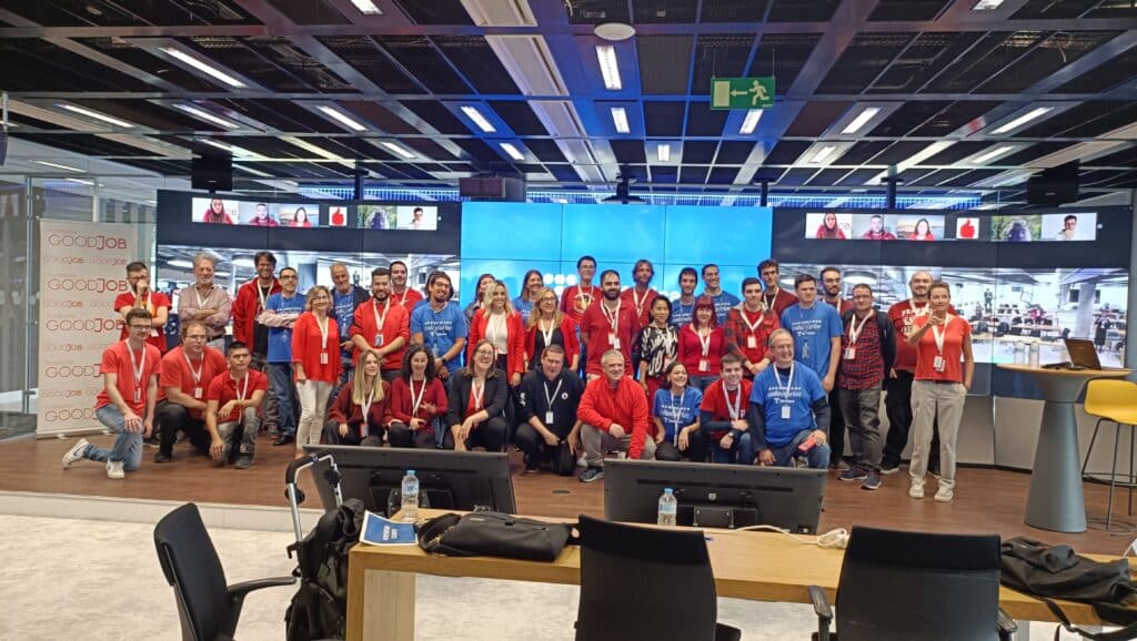 Grupo de participantes y organizadores del programa IMPACT#include posando en un auditorio tecnológico con pantallas grandes en el fondo y logotipos de GoodJob visibles en el lateral